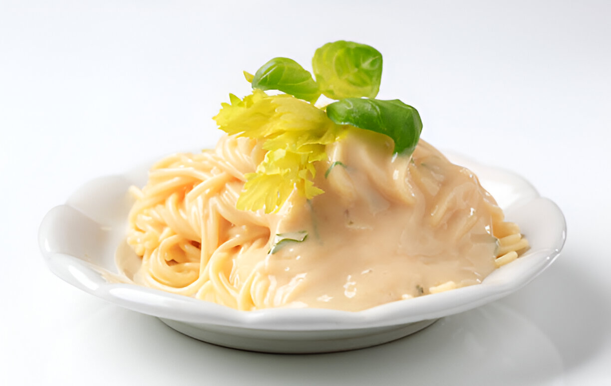 Plate of spaghetti topped with a creamy sauce and garnished with fresh leaves.