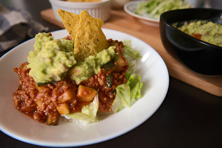 A delicious plate of nachos topped with guacamole and chili, served on a bed of lettuce.
