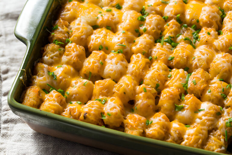 A close-up of a baked dish topped with golden melted cheese and green herbs, featuring tater tots.