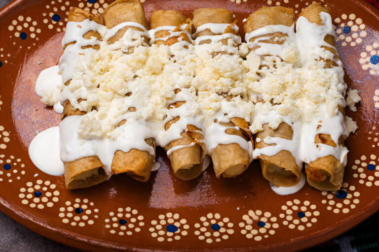 A plate of crispy flautas topped with sour cream and crumbled cheese.