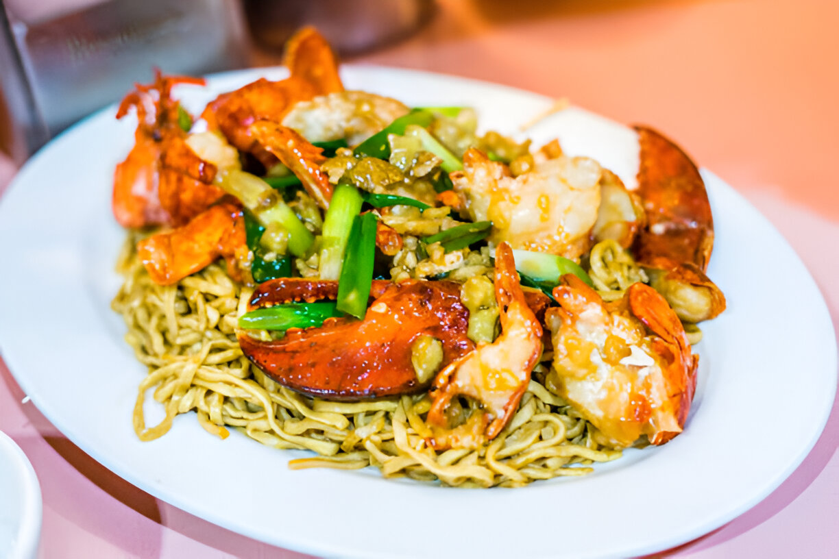 A plate of stir-fried noodles topped with succulent lobster and shrimp, garnished with green onions.