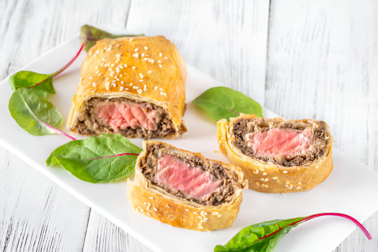 A plate of sliced beef Wellington, showcasing the flaky pastry and pink beef filling, garnished with fresh greens.