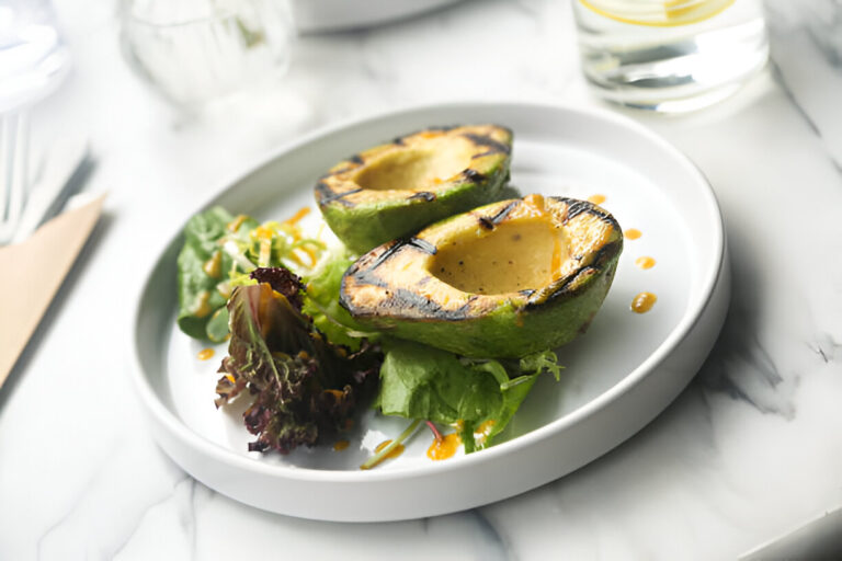 Grilled avocado halves served on a plate with salad greens and a drizzle of sauce.