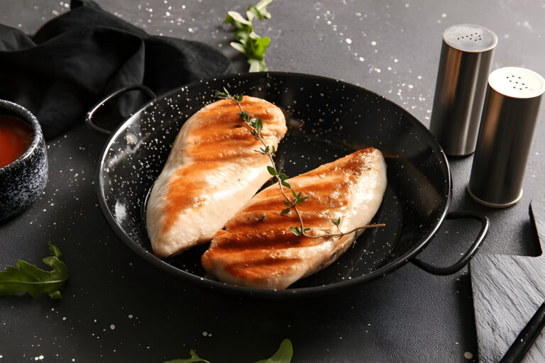 Two grilled chicken breasts garnished with thyme served in a black dish on a dark countertop.
