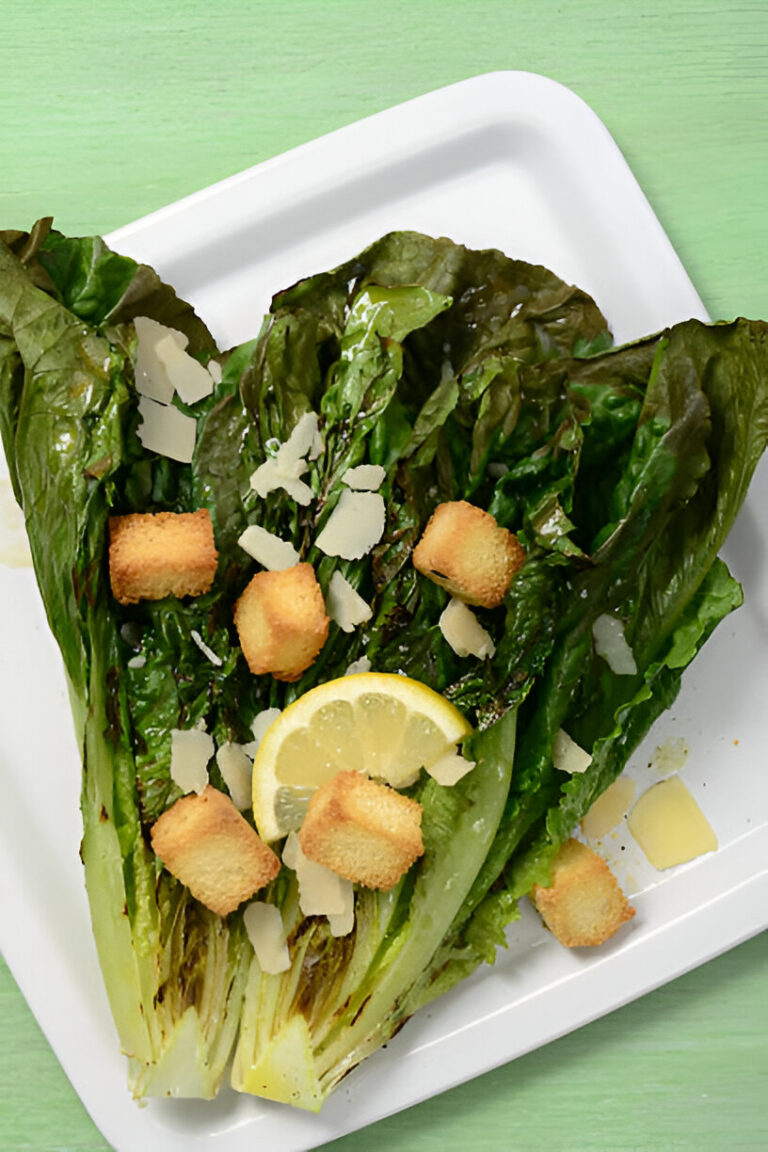 Fresh romaine lettuce topped with croutons, shaved cheese, and lemon slices on a white plate.