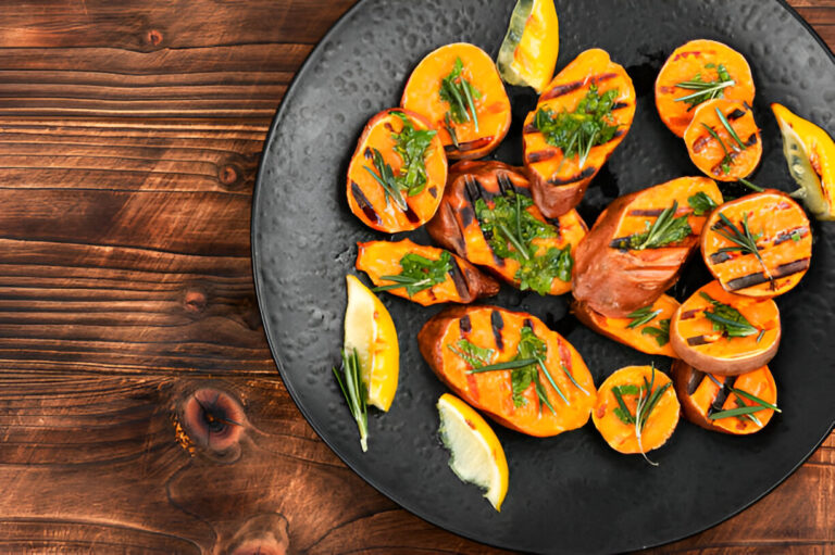 Grilled sweet potatoes garnished with herbs and lemon slices on a black plate