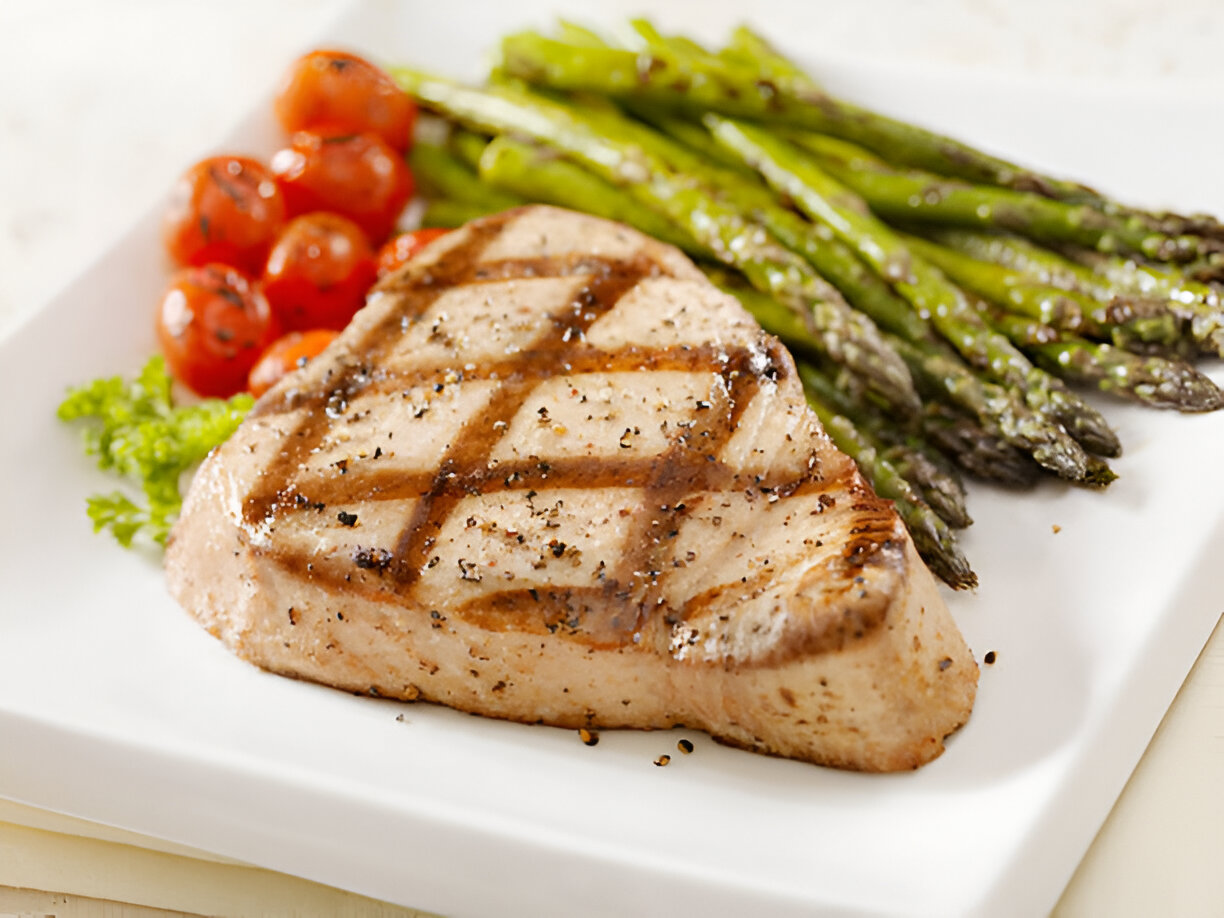 Grilled fish steak served with asparagus and cherry tomatoes on a white plate