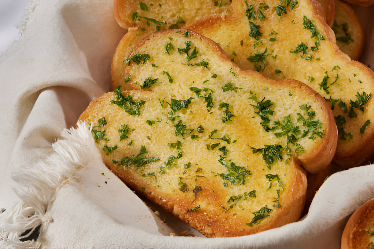 Garlic bread slices topped with parsley in a cloth-lined basket.