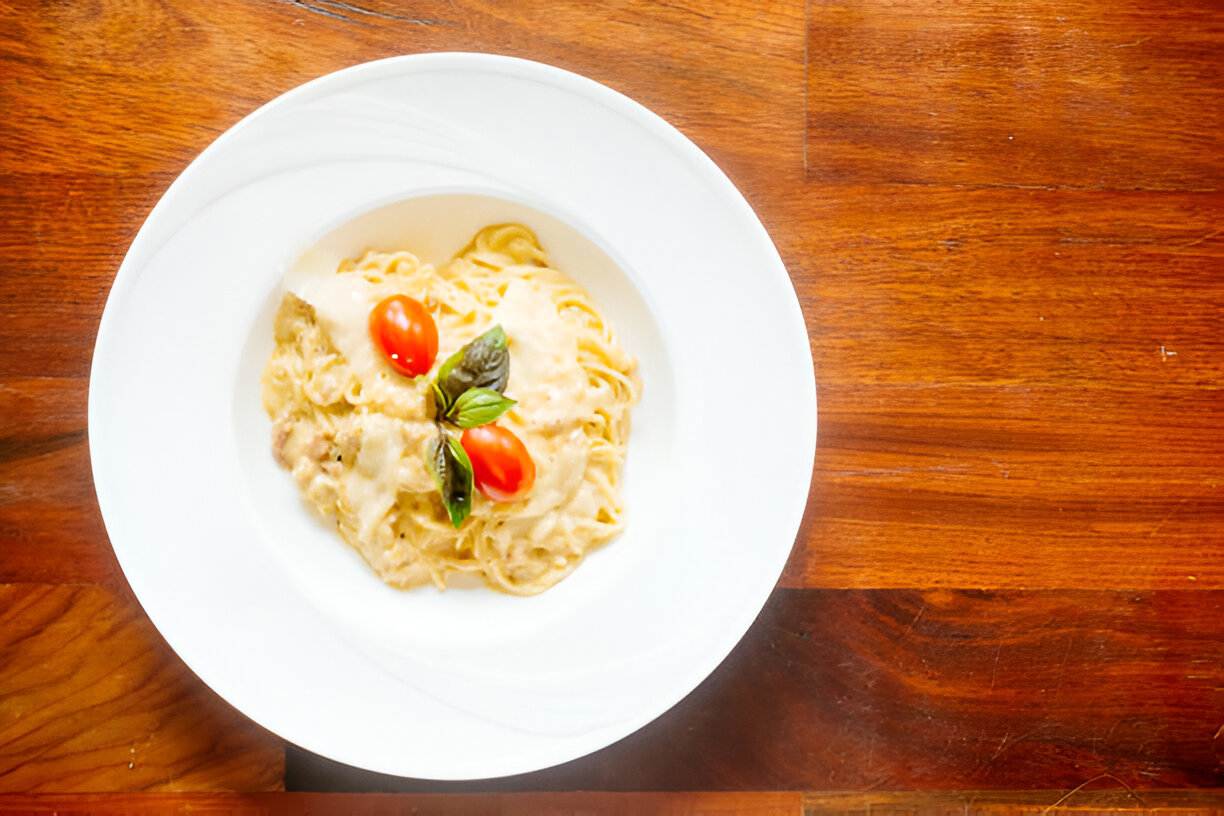 A plate of creamy pasta garnished with cherry tomatoes and basil leaves on a wooden table.