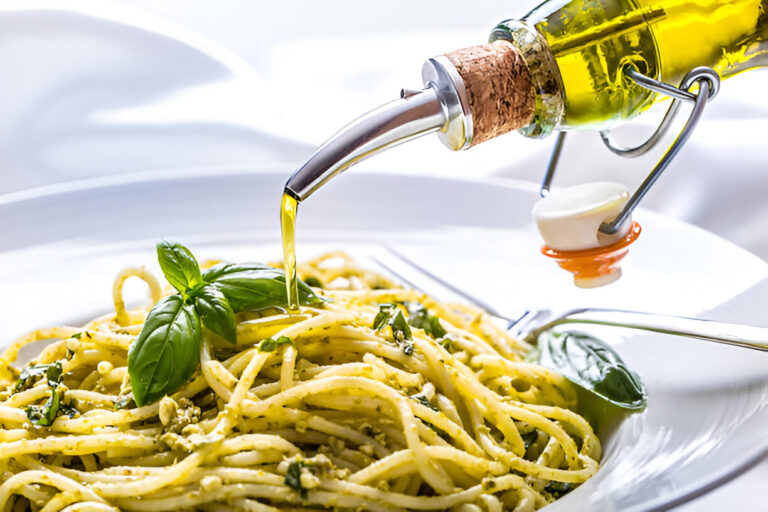 A plate of spaghetti topped with fresh basil leaves, with olive oil being drizzled over it from a bottle.