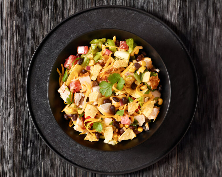 A colorful bowl of salad with chicken, black beans, corn, tomatoes, avocado, and tortilla strips served on a black plate.