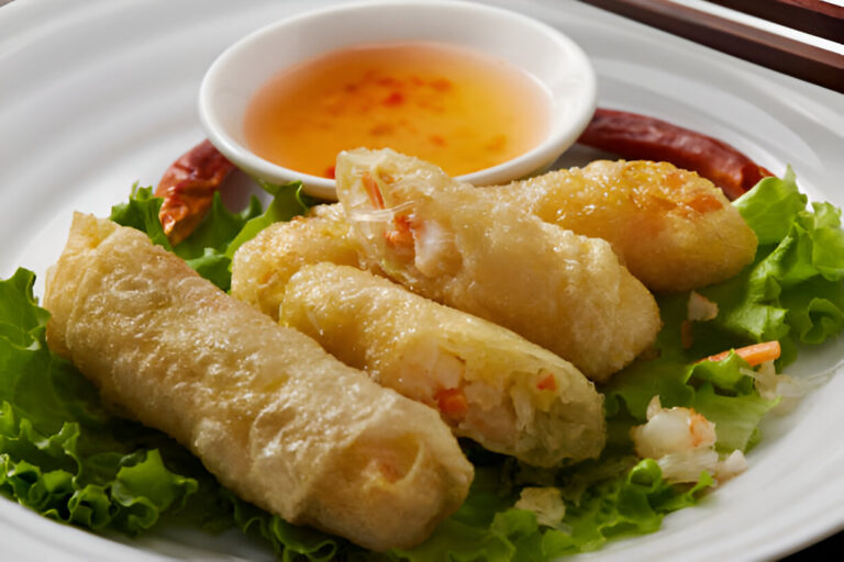 Golden fried spring rolls served on a bed of lettuce with a small bowl of dipping sauce and chili.