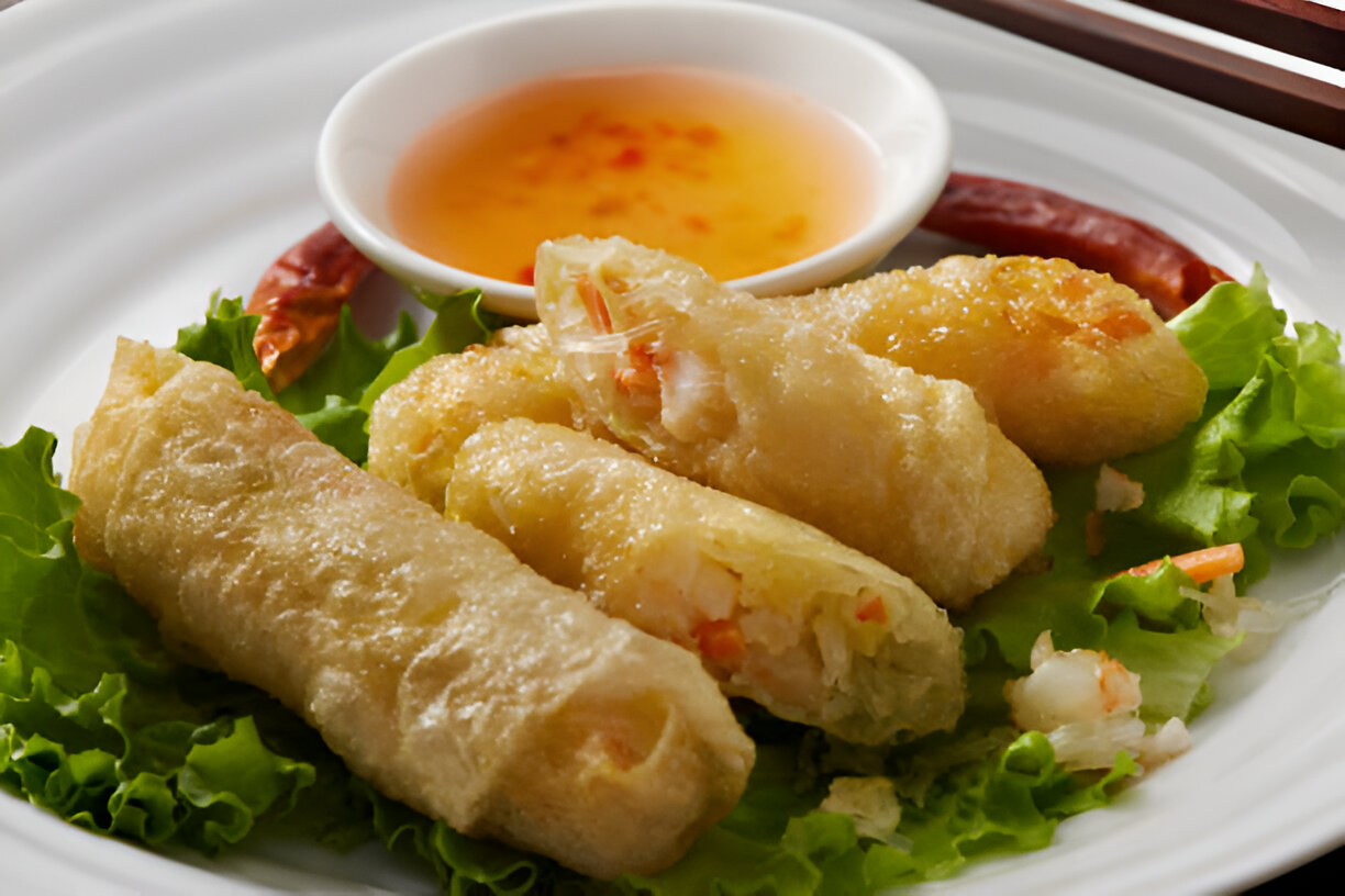 Golden fried spring rolls served on a bed of lettuce with a small bowl of dipping sauce and chili.