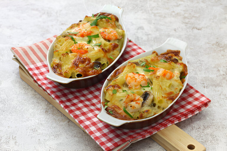 Two baked seafood pasta dishes in white serving bowls on a red and white checkered cloth.