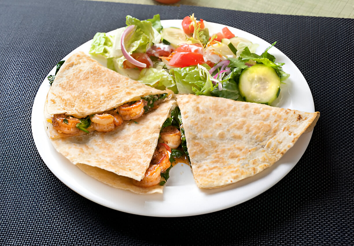 A plate with shrimp quesadilla and fresh salad on a textured black table surface.
