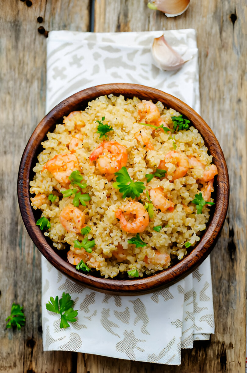 A wooden bowl of quinoa mixed with shrimp and garnished with fresh parsley, placed on a decorative napkin.