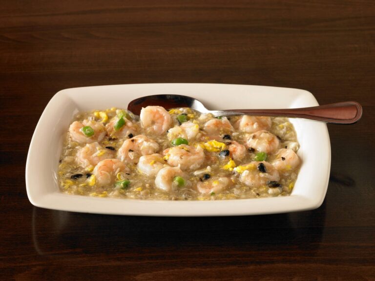 A plate of shrimp and egg dish with green peppers and black beans served on a wooden table, accompanied by a spoon.